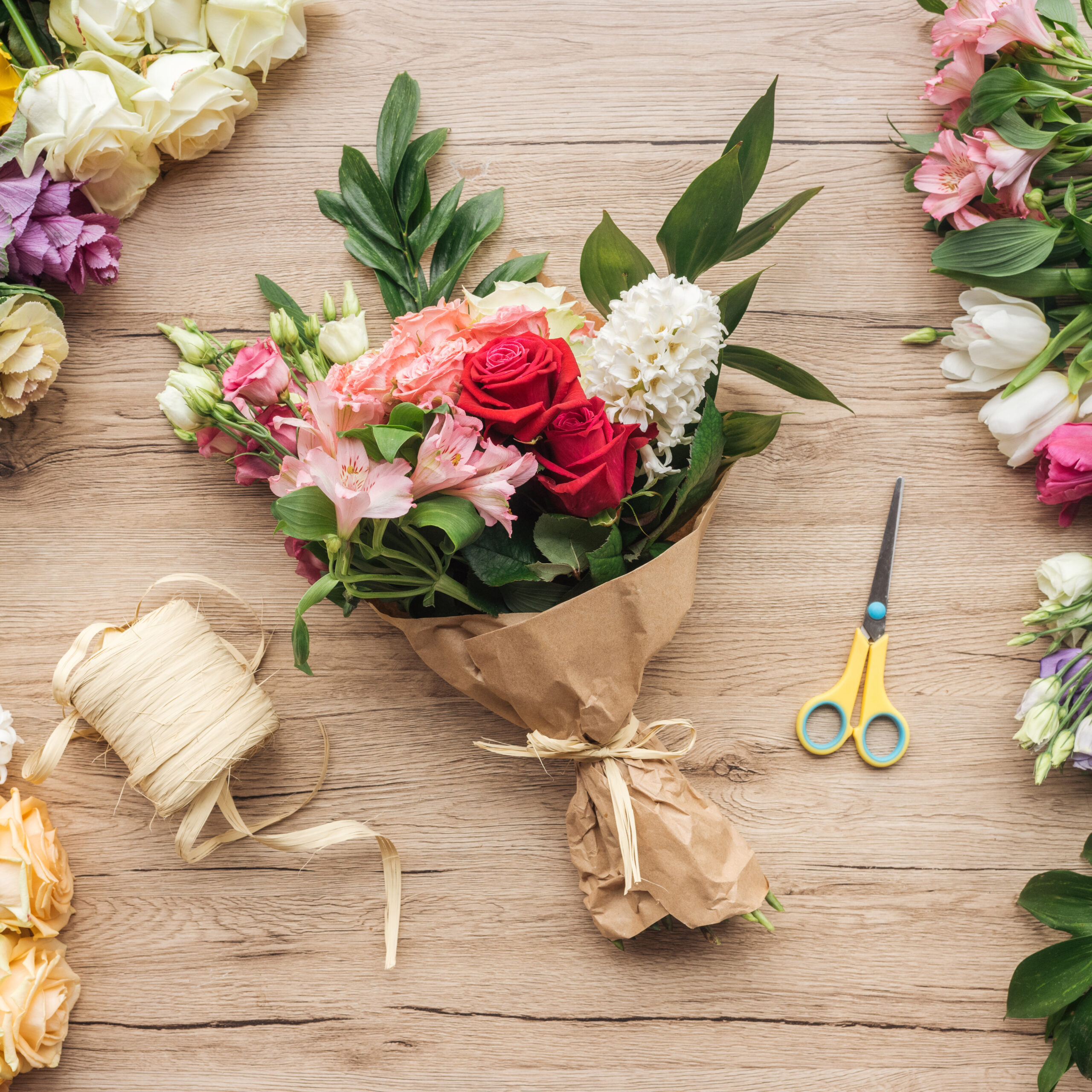 Top view of flower bouquet in paper wrapper and scissors on wood Top view of flower bouquet in paper wrapper and scissors on wooden surface